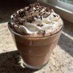 A glass of rich, blended frozen hot chocolate topped with whipped cream and chocolate shavings.