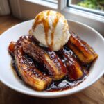 Close-up of caramelized bananas foster topped with a scoop of vanilla ice cream and caramel drizzle.