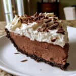 A decadent slice of Christmas chocolate cream pie featuring a thick chocolate filling, whipped cream topping, and chocolate shavings.