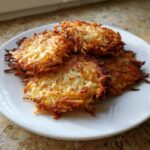 A stack of three golden-brown, crispy potato latkes served on a white plate.