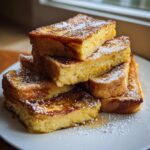 A tall stack of thick-cut, golden brown French toast dusted heavily with powdered sugar.