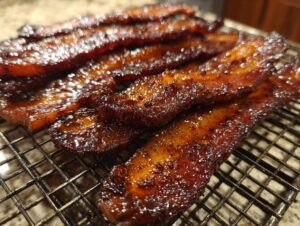 Several strips of thick, caramelized Millionaire bacon resting on a wire cooling rack, showing a glossy, dark glaze.