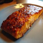 Close-up of a perfectly cooked, glazed salmon fillet with a dark, savory crust, ready to eat.