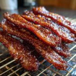 Close-up of shiny, candied Millionaire bacon strips cooling on a gold wire rack.