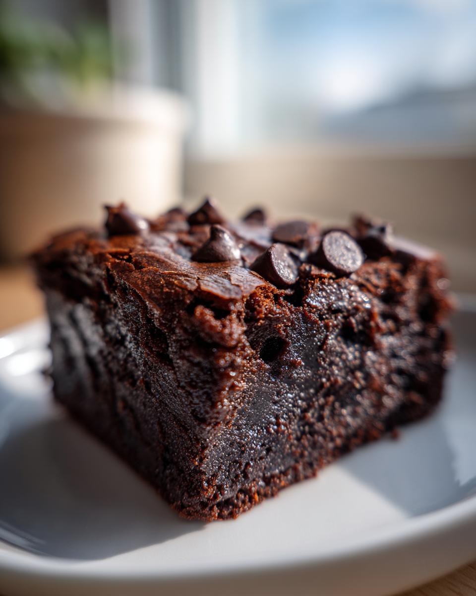 Close-up of a rich, fudgy slice of sweet potato brownies topped with chocolate chips on a white plate.