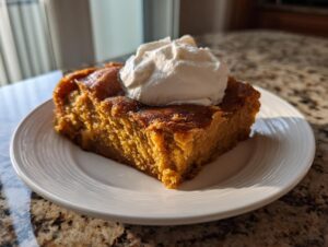 A square slice of rich, orange pumpkin dump cake topped with a dollop of white whipped cream on a white plate.
