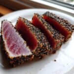 Four thick slices of perfectly Seared Ahi Tuna, crusted with black and white sesame seeds, showing a rare, deep red center.