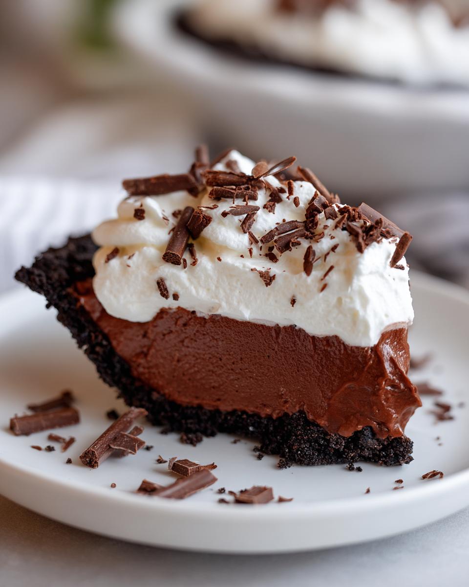 A close-up of a slice of rich Christmas chocolate cream pie with a dark crust, topped with whipped cream and chocolate shavings.