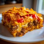 Close-up of a hearty slice of Dorito Casserole featuring layers of seasoned beef, cheese, and a crunchy Dorito chip topping.