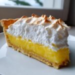 A close-up slice of lemon meringue pie showing thick yellow filling, golden crust, and perfectly toasted meringue peaks.