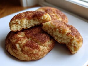 Close-up of soft, chewy Snickerdoodle cookies, one broken in half showing the fluffy interior texture.