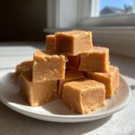 A tempting stack of creamy, square-cut peanut butter fudge cubes piled high on a white plate.