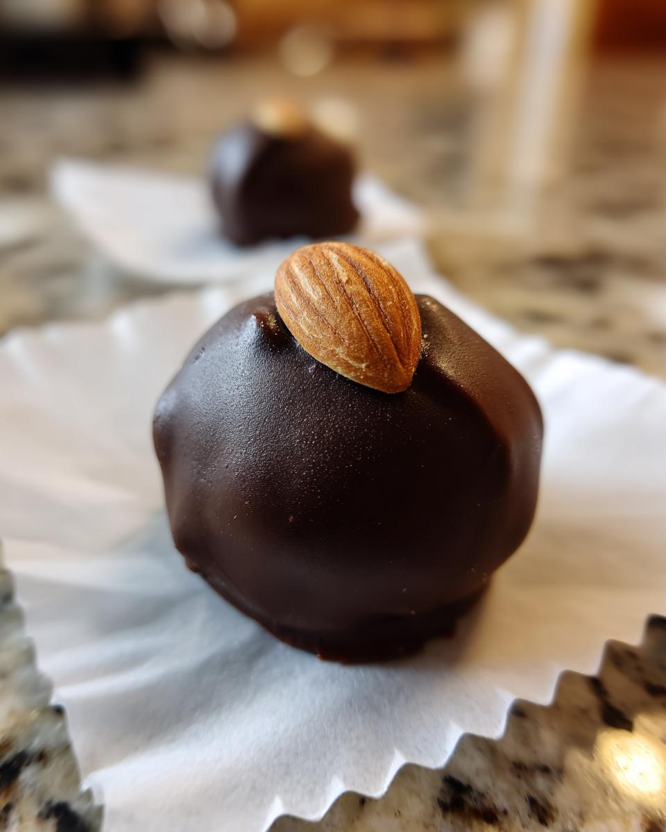 A close-up of a rich, dark chocolate coated almond joy truffles topped with a whole almond.