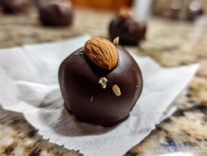 A close-up of one rich, dark chocolate Almond Joy Truffle, topped with a whole almond.