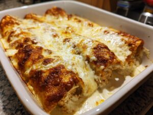 Close-up of freshly baked chicken enchiladas covered in bubbly, browned cheese in a white baking dish.