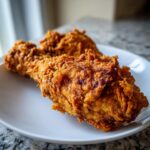 Close-up of a perfectly cooked, crispy fried chicken drumstick on a white plate.