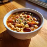 Close-up of a white bowl filled with hearty pasta fagioli soup, showing ditalini pasta, beans, and vegetables.