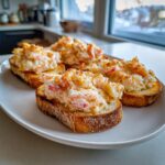 Four pieces of baked shrimp toast with creamy shrimp topping served on a white plate.