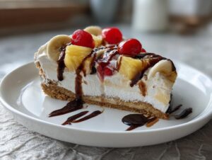 A decadent slice of banana split cake featuring whipped cream, fruit, and chocolate syrup on a white plate.