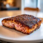 Close-up of a thick, perfectly cooked blackened salmon fillet resting on a white plate.