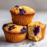 Three golden-brown blueberry protein muffins stacked, one broken open to show the moist interior.