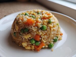 A perfectly molded serving of cauliflower fried rice mixed with bright green peas and diced orange carrots.