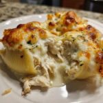 A close-up of baked chicken alfredo stuffed shells overflowing with creamy filling and topped with melted, browned cheese.
