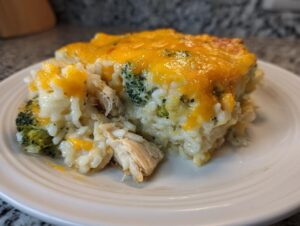 A generous serving of creamy chicken broccoli rice casserole topped with melted cheddar cheese on a white plate.
