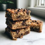 A stack of three rich, chewy chocolate chip oatmeal bars, with one bar resting beside them.