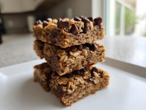 A stack of three homemade oatmeal bars topped with chocolate chips resting on a white plate.