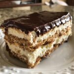 A close-up slice of chocolate eclair cake showing layers of graham crackers, cream filling, and chocolate glaze.