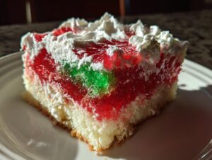 Close-up of a slice of christmas poke cake featuring layers of white cake, red and green jello, topped with whipped cream.