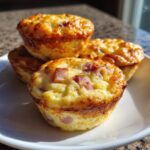 Four golden brown cottage cheese egg cups with visible ham pieces stacked on a white plate.