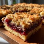 A close-up shot of a single square of cranberry crumble bars showing the thick, jammy filling and golden crumb topping.
