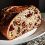 Close-up of a slice of homemade cranberry walnut bread showing the open crumb texture filled with walnuts and dried cranberries.