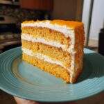 A tall slice of orange Creamsicle Cake showing multiple layers of orange sponge and white frosting.