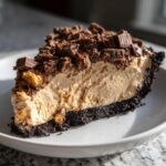 A generous slice of creamy butterfinger pie featuring a dark chocolate crust and topped with crushed Butterfinger pieces.