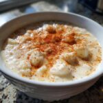 Close-up of a creamy, white bowl of crab soup topped generously with bright red paprika seasoning.