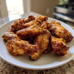 A pile of golden brown, crispy chicken wings served on a white plate, ready to eat.