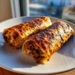 Two perfectly golden and crispy chimichangas filled with seasoned meat and cheese, served on a white plate.