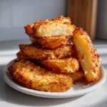 A tall stack of golden-brown, crispy potato wedges piled high on a white speckled plate.