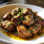Close-up of tender crockpot steak bites coated in a rich, garlicky butter sauce and topped with fresh parsley.