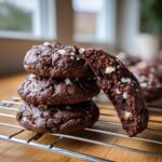 A stack of three rich, dark double chocolate peppermint cookies topped with sea salt, with one cookie broken open to show the fudgy interior.