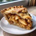 Close-up of a thick slice of apple pie showing flaky crust and caramelized apple filling.