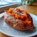 A perfectly cooked, fluffy baked sweet potato split open and topped with coarse sea salt and black pepper.