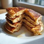 Close-up of a stack of fluffy banana pancakes cut open to show the moist interior, drizzled with syrup.