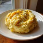 A serving of fluffy mashed potatoes topped with melted butter and dried herbs on a white plate.