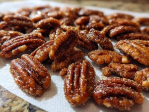 A close-up, shallow depth-of-field photo of freshly made candied pecans cooling on a white paper towel.
