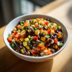 Close-up of vibrant cowboy caviar featuring black beans, corn, red peppers, and cilantro in a white bowl.