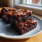 Close-up of fudgy oreo brownies stacked on a plate, showing a shiny, crackly top.